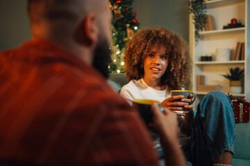 Young couple relaxing on sofa drinking coffee by christmas tree