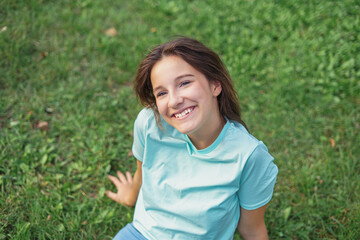 Fototapeta premium Portrait of a cute girl sitting in a park on green grass summertime