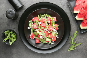 Delicious watermelon salad with feta cheese, cucumber and arugula on grey textured table, flat lay