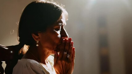 A woman prays with her hands clasped, bathed in soft light, conveying devotion, peace, and spirituality in a reflective moment.