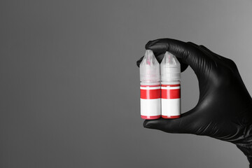 Professional cosmetologist holding bottles of pigments for permanent makeup on grey background,...