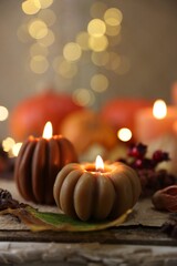 Burning candles in shape of pumpkins and autumn decor on table, closeup