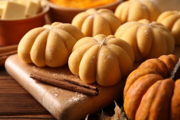 Raw pumpkin shaped buns and ingredients on wooden table, closeup