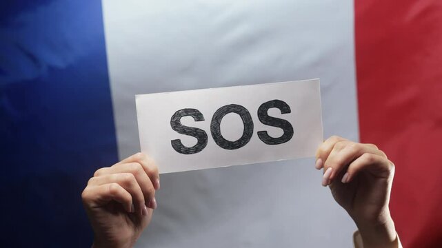 Female hands with SOS, alarm, emergency card on french National flag background. France labor exploitation, migrants, refugees, human resources, request for help, environmental care