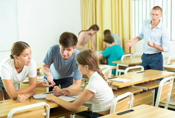 Focused teenagers working in small groups during lesson at college, discussing assignment given by teacher. Active learning concept