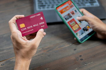 Showing a man holding a credit card and a smartphone for online shopping, sitting at a wooden table. ecommerce concept