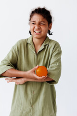 Young boy looking contemplative while holding an orange and touching his face thoughtfully