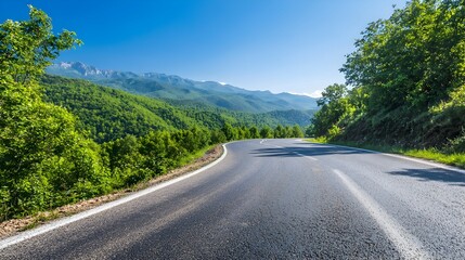 Winding asphalt road snaking through a lush green forest at the base of majestic mountains framed by a clear blue sky  This picturesque scene offers a scenic journey through the natural landscape