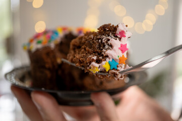 Bocado de pastel de chocolate decorado con estrellas de colores y fondo de luces desenfocadas