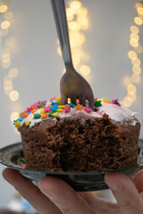 pastel de chocolate mordido con tenedor clavado y fondo decorativo de luces desenfocadas