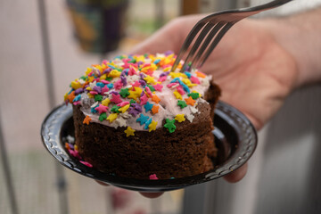 mano sosteniendo plato con pastel de chocolate con decorado de estrellitas de colores y tenedor 