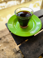 a cup of hot coffee in a small green saucer on a wooden bench