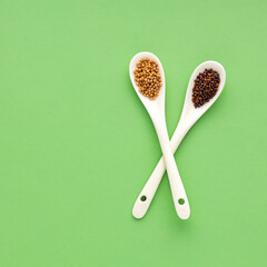 Brown and yellow mustard seeds in two spoons.