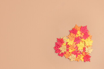 Colorful autumn leaves forming a heart on a beige backdrop, creating a cozy Thanksgiving...