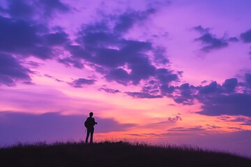 Fototapeta premium A striking silhouette of a person standing on a hill against a purple sunset, symbolizing contemplation, solitude, and the beauty of nature's quiet moments.
