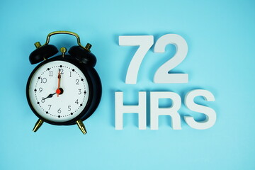 72 Hrs alphabet letters and alarm clock top view on blue background