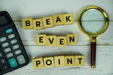 Break Even Point with wooden blocks alphabet letters and magnifying glass, calculator top view on wooden background