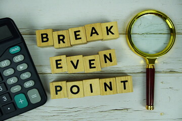 Break Even Point with wooden blocks alphabet letters and magnifying glass, calculator top view on wooden background