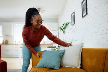 Happy black woman decorating her sofa with pillows.