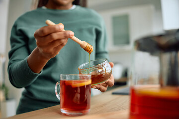 Close up of black woman adding honey into cup of tea.