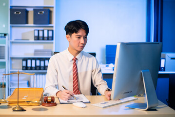 Young Asian lawyer at desk with legal scales and gavel, writing documents in office, offering legal services