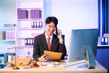 Young Asian lawyer at desk with legal scales and gavel, writing documents in office, offering legal services