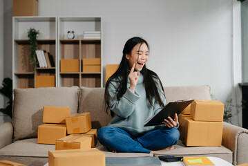 woman using smartphone or tablet taking receive and checking online purchase shopping order to preparing pack product box. .