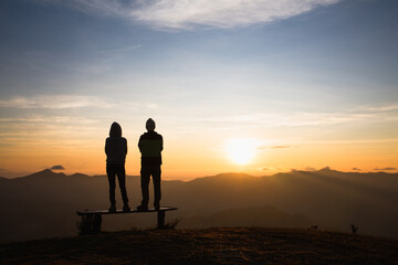 Silhouette of a couple on a mountaintop. Happy young female and male contemplating the scenic sunrise. Man and woman standing on mountain, Couple Looking at Sunset.