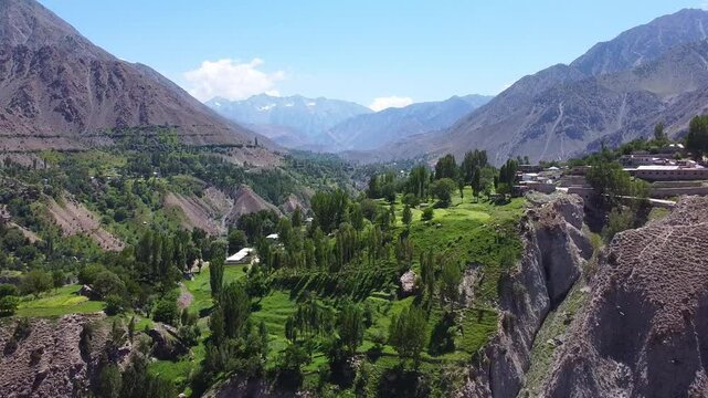 Pull away aerial shot of astore valley in Pakistan, showcasing vibrant landscapes and dramatic mountain ranges under a clear blue sky, highlighting the region's natural beauty and serene environment