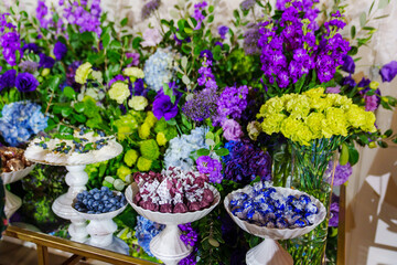 Table with sweets and cakes decorated with bouquets of purple flowers. 