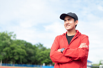 Handsome Asian man in sportswear posing with arms crossed in stadium Handsome male athlete looking and smiling at the camera. stadium background Active living concept Sports and recreation, exercise.