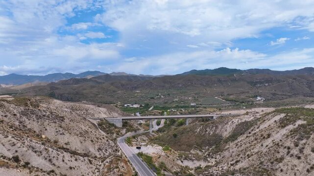 Flight reverses from a pristine newly constructed rail bridge revealing a road below and a vast rugged background landscape under a searing hot sky Sorbas Almeria Espana Spain