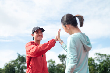 Young Asian couple wearing blue and red sportswear exercising. They are both high five. Outdoor exercise. Exercise in the stadium maintaining health exercise active living