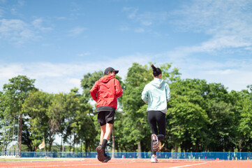 Obraz premium A young Asian couple wearing blue and red sportswear, the two of them jogging together. Ready to talk while running outdoor exercise Exercise in the stadium maintaining health exercise active living