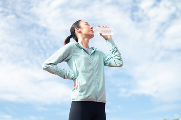 Asian woman wearing blue sportswear Stand and drink water after exercising. outdoor exercise...