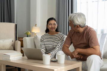 Cheerful middle aged couple in living room laptop and coffee cups on table