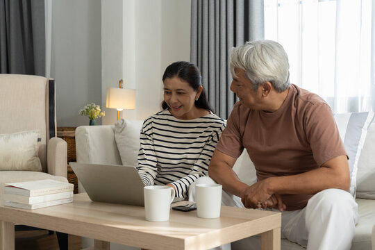 Cheerful middle aged couple in living room laptop and coffee cups on table