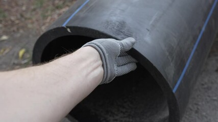 A man's hand in a gray work glove runs along the edge of a large diameter black plastic pipe. Close-up. Sewer pipes, water pipes, heating pipes. High quality 4k footage