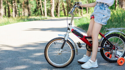 Fototapeta premium Child riding a bike in summer park. Children learning to drive a bicycle on a driveway outside. Kid riding bike. Child on bicycle, bike outdoor close up