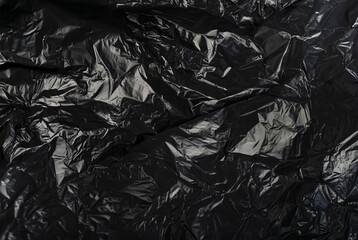 Close-up of a crumpled black plastic material with irregular folds and shiny surface.