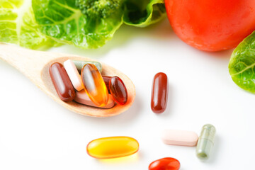 Wooden spoon with herbal pills capsules, dietary supplements vitamins on vegetables background