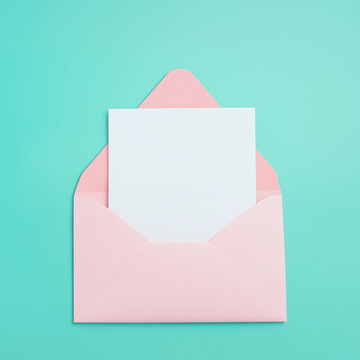 Open a light pink envelope with a white card on a turquoise background, in a flat lay arrangement. Pastel colors. Minimalism