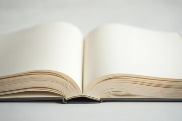 Fototapeta premium An open, thick book placed on a simple beige surface. The white pages are blank, catching soft