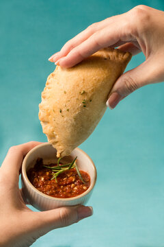 Hands dipping a meat pie in salsa