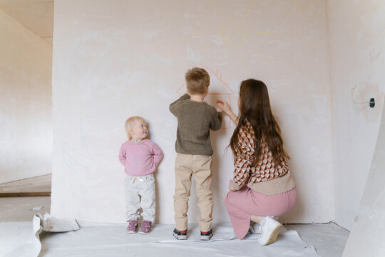 Children draw a house with chalk on a concrete wall in a house