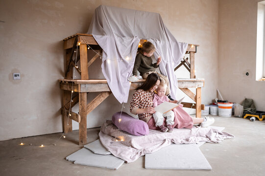 A young woman reads a story to her children in a house made of sheets