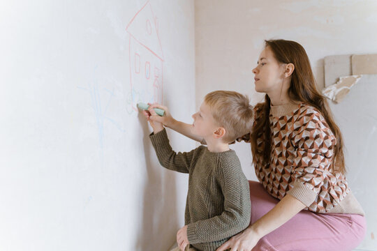 Mom and son draw a house with chalk on a concrete wall amid renovation