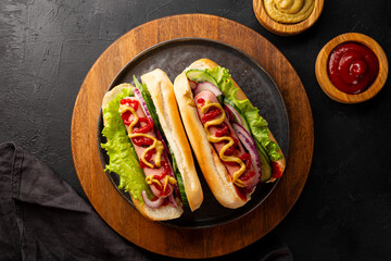 Homemade hot dogs with sausage, green salad, cucumber and red onion on the black background top view