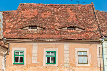 A close-up view of a traditional building facade in Sibiu, Romania, featuring a red tiled roof with a distinctive arched shape. 