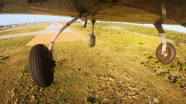Light three wheels airplane approaching to the airport's runway overhead the grass field and landing. View from the bottom of aircraft.